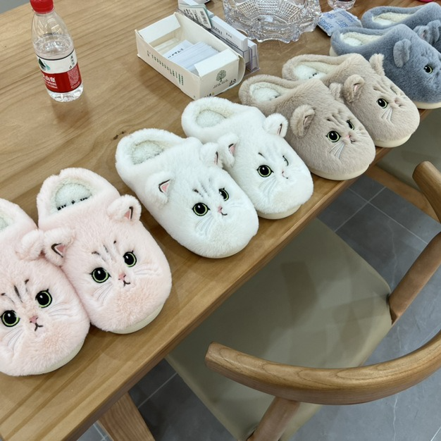 Cat face plush slippers in pink, white, brown and grey on a table