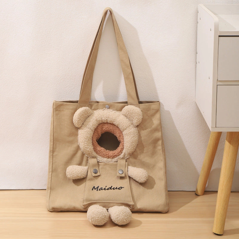 Khaki canvas tote-style cat carrier with a teddy-bear head opening and dangling legs beside a white drawer unit