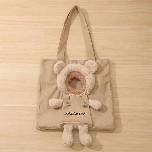 Khaki canvas tote-style cat carrier laid flat on a wood surface, showing the bear-head opening and dangling teddy legs