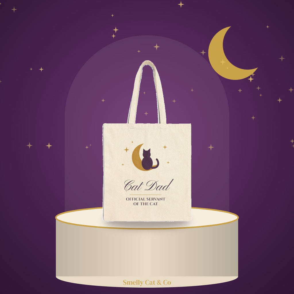Cat Dad tote bag on a cream podium under a gold moon (product photo on an illustrated background)