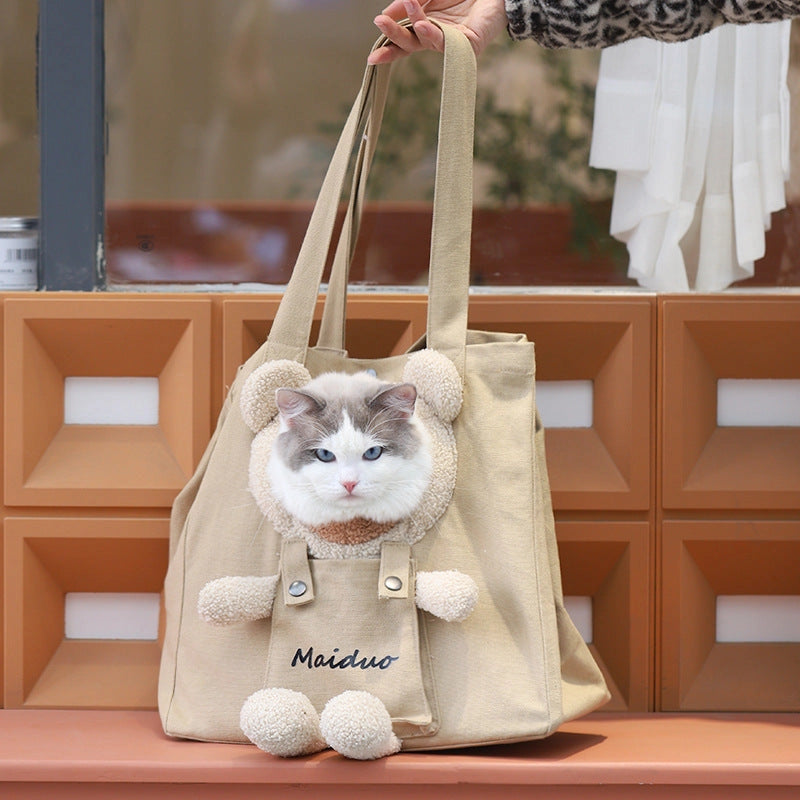 Hand holding up the khaki canvas cat tote by its handles, with a white and gray cat's head looking out of the bear opening